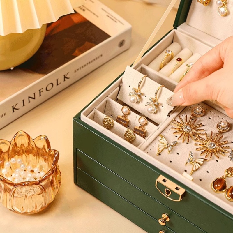 Close-up of velvet-lined earring panel and ring rolls inside a green jewelry box with lock